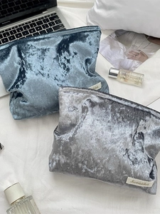 Velvet makeup storage bags in grey and blue with zipper closure on a white bed