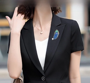 Detailed close-up of a peacock feather brooch with enamel inlay and pearl on a black blazer