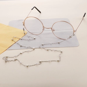 Detail showing silver chain with white pearls and polished metal cubes on glasses