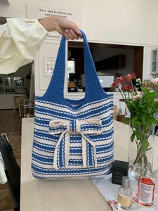 Detail of blue and beige striped knit tote bag featuring a large decorative soft bow