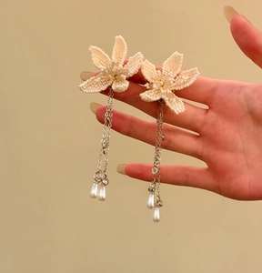 Hand zeigt Details der weißen Perlenblumen-Ohrringe mit langen Perlenquasten