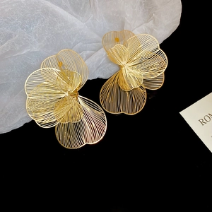 Détail macro de boucles d'oreilles fleurs ajourées dorées montrant la texture des pétales