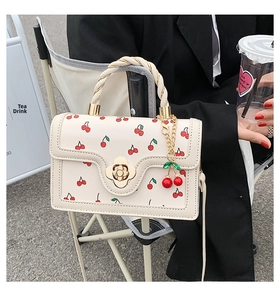 Detail of white cherry print handbag with golden flower clasp and cherry pendant