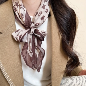 Close-up of beige silk scarf necklace with vintage brown pattern on khaki coat
