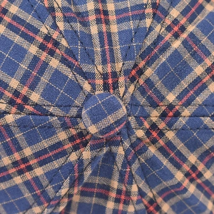 Dettaglio ravvicinato della trama del tessuto scozzese blu e beige e del bottone del cappello
