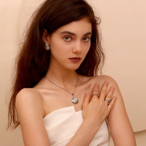 Close-up of model wearing silver shell necklace and matching earrings set on neutral background