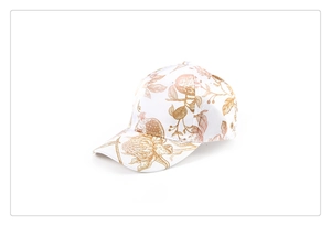 Dettaglio del cappellino bianco con motivi botanici dorati e stampa floreale