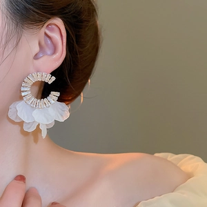 Close-up of C-shaped gold earrings with zircon crystals and white petal tassels on a model
