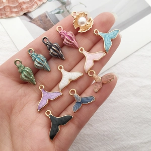 Hand holding colorful enamel seashell and mermaid tail pendants with golden finish
