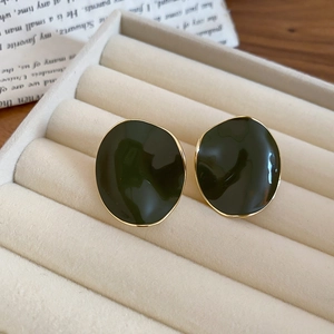 Macro shot of dark green enamel earrings with irregular gold plating on a jewelry box