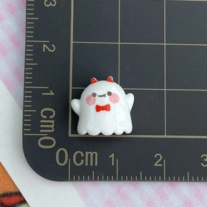 Mini glossy white resin ghost charm with red bowtie measured on a grid cutting mat