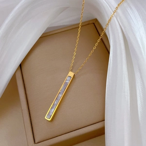 Detail of a minimalist gold necklace featuring a rectangular white shell inlay on a silk cloth