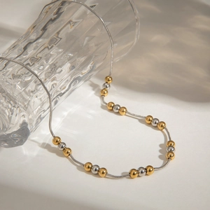 Minimalist gold and silver beaded snake chain necklace displayed on a glass surface