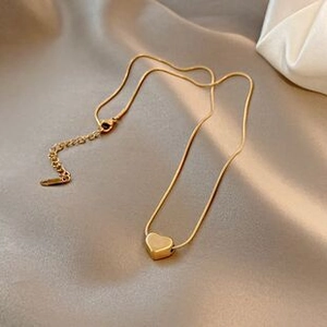 Détail du pendentif cœur doré sur une chaîne serpent posé sur un tissu en soie