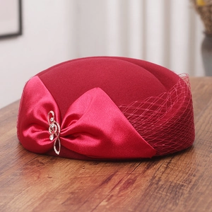 Detail of red wool pillbox hat featuring a silk bow, mesh veil, and rhinestone music brooch