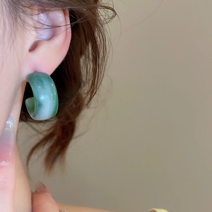 Gros plan d'une boucle d'oreille en résine verte en forme de C avec texture marbrée