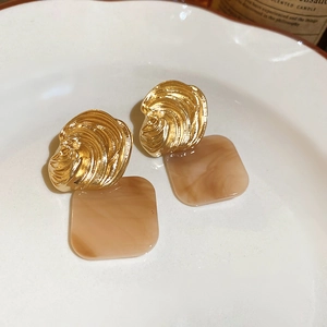 Detailed shot of retro gold shell textured metal and marble acrylic earrings on white ceramic