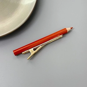 Détail de la pince à cheveux crayon rouge avec clip en métal doré pour un style créatif