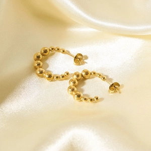 Macro detail of gold beaded semi-hoop earrings featuring alternating size beads on silk
