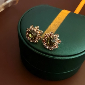 Macro detail of olive green floral stud earring with crystals on dark jewelry box
