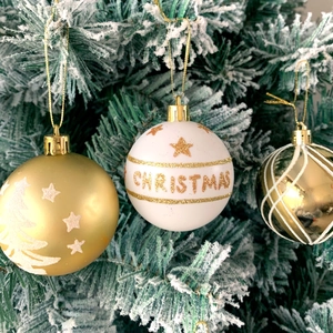 Detail of gold and white Christmas balls with stars and lettering on a snowy branch