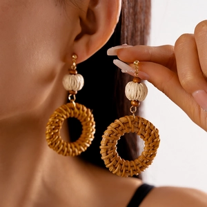 Macro detail of bohemian handmade rattan hoop earrings featuring white woven balls and wood beads