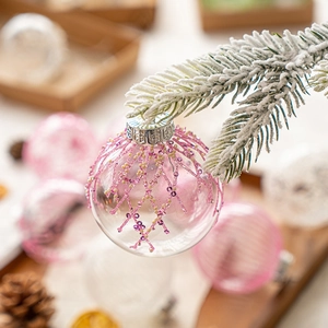 Clear Christmas tree ball with pink beads and sequins hanging on snowy pine branches