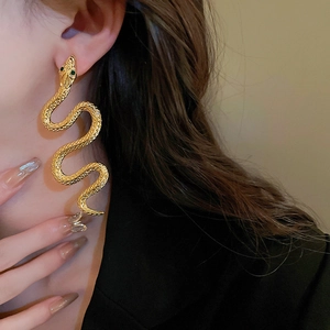 Close-up of golden snake earrings with green gemstone eyes on model with scales detail