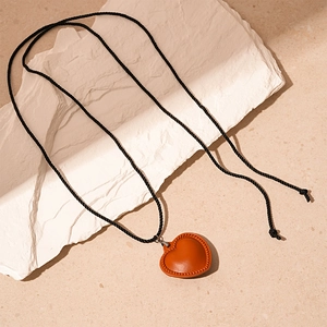 Gros plan d'un pendentif cœur en simili cuir marron avec cordon tressé noir sur pierre