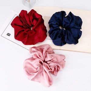 Detailed close-up of glossy satin scrunchies in red, blue and pink with elegant pleats