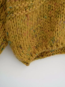 Close-up of mustard yellow tweed knit sweater showing coarse needle texture and rib hem
