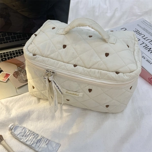 Detail of quilted cream makeup bag with heart embroidery and stylish ribbon zipper