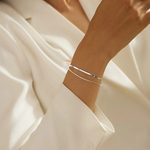 Detail of layered silver snake bone and round link chain bracelets on a woman wrist
