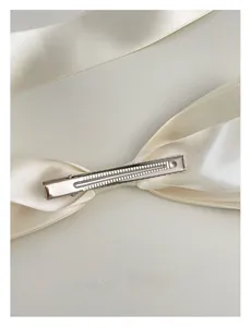 Detail of a creamy white satin bow hair clip showing the silver metal duckbill clip back