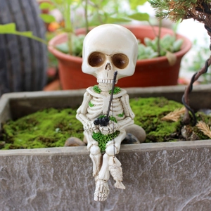 Macro shot of a resin fishing skeleton figurine with green moss details and a small fish