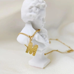Gouden roestvrijstalen ketting met letter M hanger op een witte buste standaard