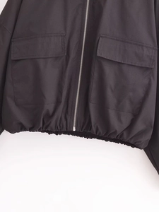 Détail d'une veste noire à capuche avec fermeture éclair argentée et grandes poches