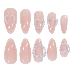 Detail of almond-shaped pink press-on nails featuring French V-tips and pearl heart accents