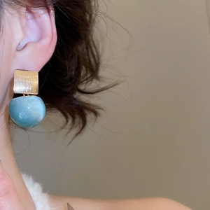 Detail of teal resin sphere earrings with brushed gold squares on a female model