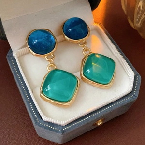 Détail de boucles d'oreilles vintage dorées avec pierres bleue et verte dans un écrin