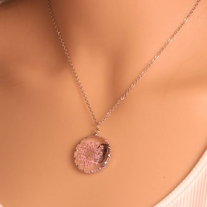 Detailed close-up of a round glass pendant with a pink dried flower on a silver chain