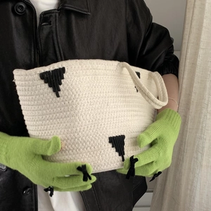Detail of cream knit handbag with black patterns held by hands in green winter gloves