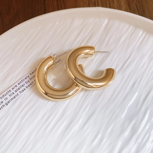 Detail of elegant gold C-shaped earrings displayed on a white textured marble dish