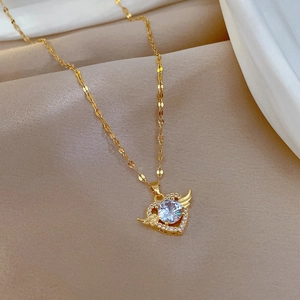 Macro view of gold heart pendant necklace with angel wings and micro-inset gemstone