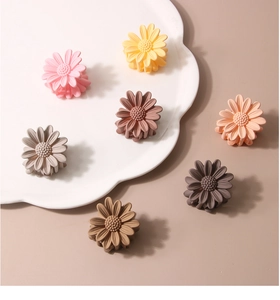 Close-up of small matte daisy hair claws in seven pastel colors on a white ceramic plate