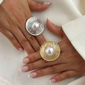 Close-up of gold and silver metallic textured rings with large faux pearls on a hand