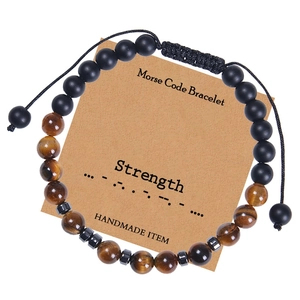 Détail du bracelet code Morse sur carte affichant le message Strength et perles d'œil de tigre