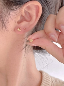 Close-up of a small golden flower stud earring shown on an ear for size perspective