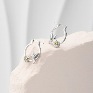 Macro shot of silver hummingbird earrings with floral details and yellow gemstones