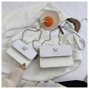 Close-up of a white leather crossbody bag with silver sequins and a butterfly metal clasp